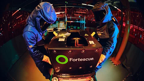 Two workers in full protective blue suits stand either side of a large EV battery (Credit: Formula E)