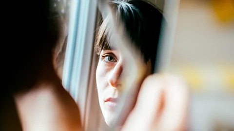 The partial reflection of a woman's face in a mirror (Credit: Getty Images)