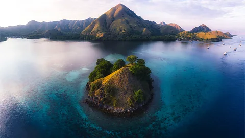 The Komodo Islands are shown from above, with a smaller island in the foreground surrounded by deep blue ocean and an island with a taller peak in the background (Credit: Alamy)