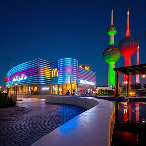 Gary He/McAtlas Night view of McDonald's lit up in blue and purple lights with Kuwait Towers glowing green and red in background (Credit: Gary He/McAtlas)