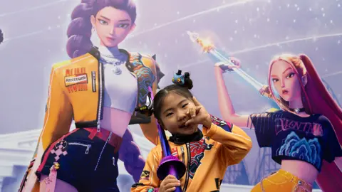 EPA A girl in a KPop Demon Hunters costume standing in front of a still from the film