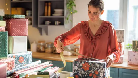 A woman at home in her ktchen wraps Christmas presents on a table