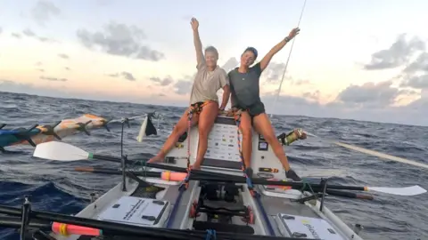 Two women pose for a celebratory photo on board their boat on the Pacific Oean.