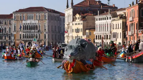 A boat carries a "Pantegana", the big rat, as revellers row during the masquerade parade on the Grand Canal during the Venice Carnival, in Venice, Italy.