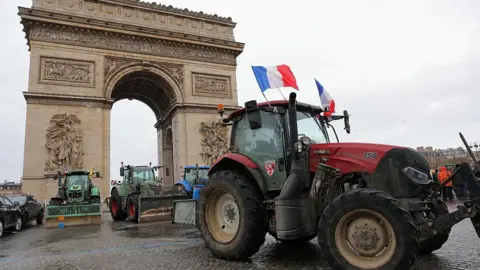 AFP via Getty Images Several tractors, including a red tractor flying French flags, are parked in front of the Arc de Triomphe in Paris.