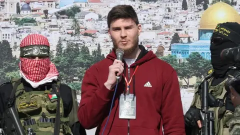 Masked Palestinian gunmen stand either side of Israeli hostage Sasha Troufanov during his release
