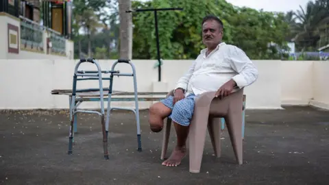Strike Out Snakebite Devendra is sitting on a chair, his amputated leg is visible under his dhoti - a long piece of cloth worn by men in India.