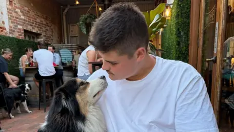 Constable Jack Hibbert dressed in a whiteT-shirt looking down at a dog and sitting in a restaurant.