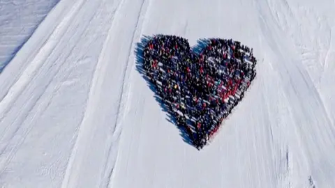 Skiers form the shape of a heart on a ski field from birds-eye-view