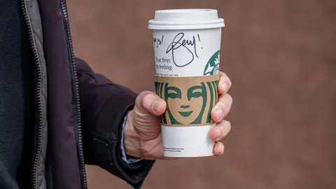A customer carries a Starbucks cup with a handwritten message written on it outside one of the company's coffee shops in San Francisco, California, US.