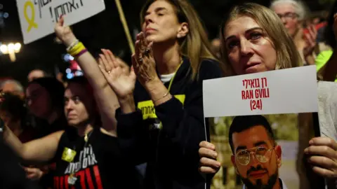 A woman holds a picture of Ran Gvili, the last dead Israeli hostage in Gaza, at a rally in Hostages Square in Tel Aviv, Israel (29 November 2025)