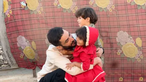 A Palestinian man embraces his smiling children in Gaza.