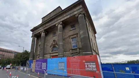 General view of a the old Curzon Street Station building which has colourful shields with the words Curzon Street a new cultural hub and metal barriers