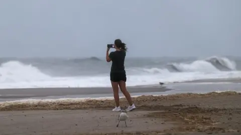 A woman takes a picture on her phone of the ocean as large waves from Hurricane Erin keep swimmers away in Seaside Heights, New Jersey. 