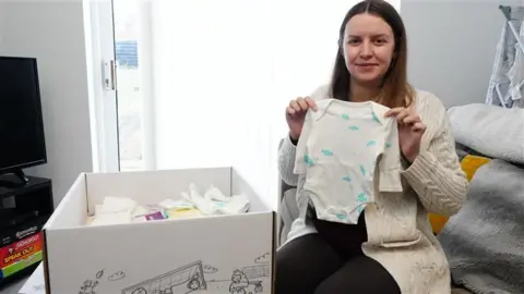 Mum holding up a babygro next to a baby bundle box