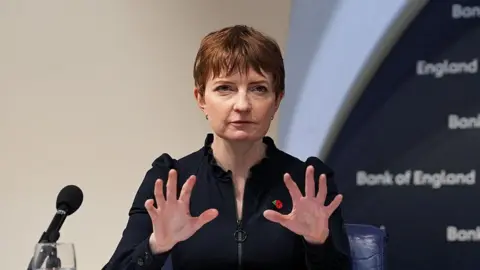 Bank of England deputy governor Clare Lombardelli addresses a press conference and gesticulates with both hands as she speaks.