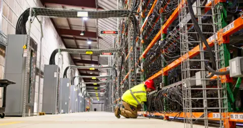 Getty Images A technician wearing PPE working on racks of equipment in a data center for cryptocurrency mining, cloud services and AI computing in a large, temperature controlled warehouse in a remote location in Stutsman County, North Dakota.