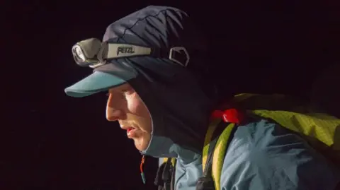 Pawel Cymbalista is pictured at night-time in running gear. He has the hood of his blue jacket pulled over a cap. He is also wearing a head torch.