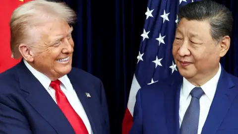 U.S. President Donald Trump and Chinese President Xi standing close together and turned to face each other in front of US and Chinese flags. Trump looks very happy