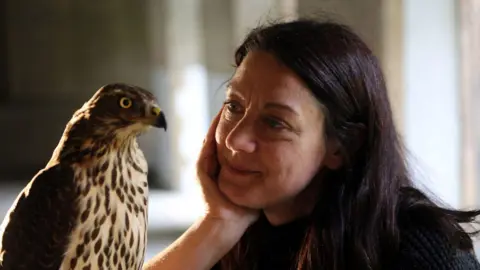 Helen MacDonald staring lovingly at her hawk. Her chin is cupped in her right hand.