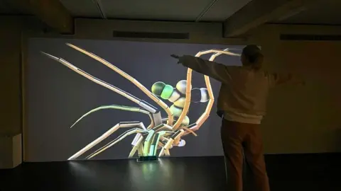 Person standing with their arms out in front of a screen with a futuristic sea creature.