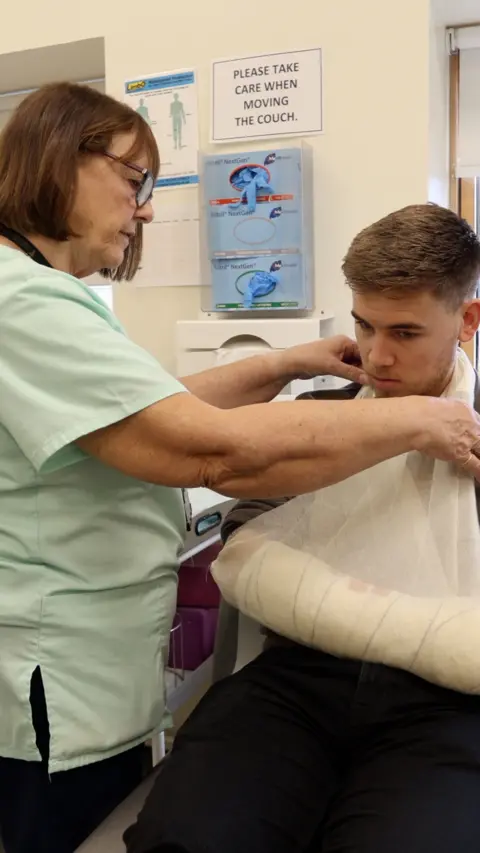 A man with his arm in a brace with a nurse seeing to him