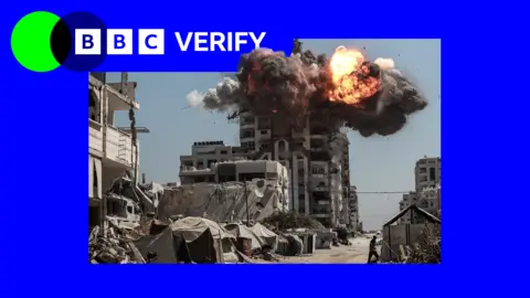 Image of a high-rise building in Gaza City, struck by an Israeli missile, black smoke and flames pouring from its upper floors. Tents and makeshift shelters are visible in th foreground along a road
