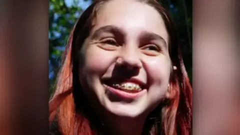 A close up image of a girl smiling. She has braces and reddy/brown hair. 