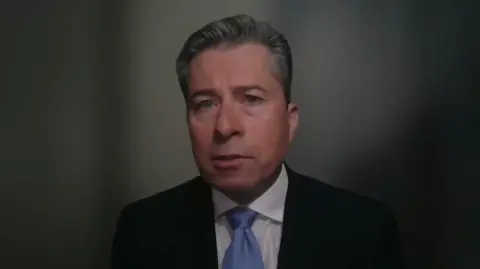 Tom Fletcher dressed in a dark suit looking pensive