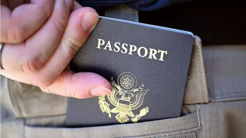 A person is seen with a US passport. Part of it is in a bag.