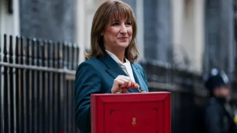 Rachel Reeves with her red Budget box standing outside 11 Downing Street, dressed in a dark green suit jacket and white blouse