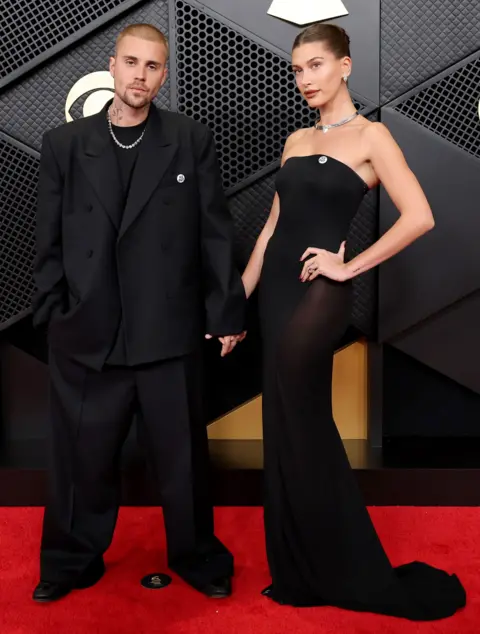 Getty Images Justin and Hailey Bieber wear black outfits with silver necklaces as they pose for photos on the red carpet at the Grammy Awards.