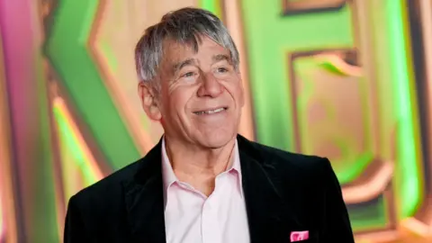 Getty Images Stephen Schwartz at the "Wicked: For Good" New York Premiere held at Lincoln Center for the Performing Arts. He wears an open-neck pink shirt and black blazer.