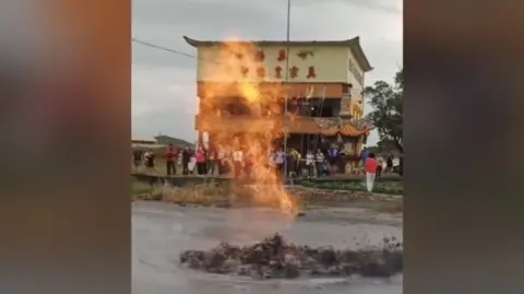 Bubbling mud and flames are seen in front of a Taiwanese temple, with a group of people gathered to watch the phenomenom.