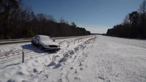 A car is on the side of the highway with snow on the ground.