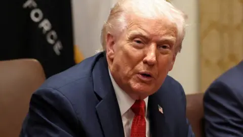 President Trump speaks while seated wearing a blue suit, white shirt and red tie.