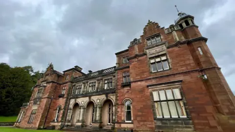 BBC An imposing red sandstone building with stone archways and ornate features. There are decorative designs above the windows and a on the upper sections of the building's facade.