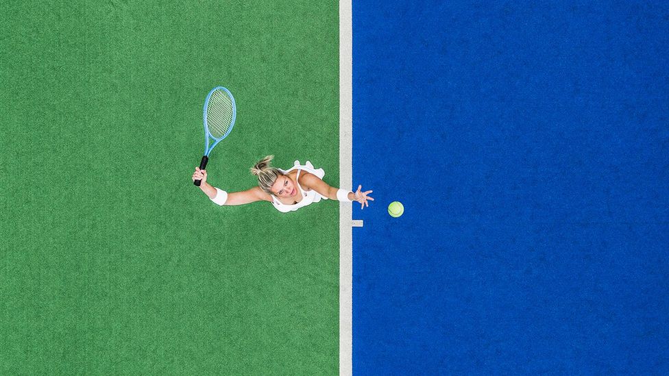 Drone shot looking down on a female about to hit a tennis serve on a two-toned blue and green tennis court (Credit: Getty Images)